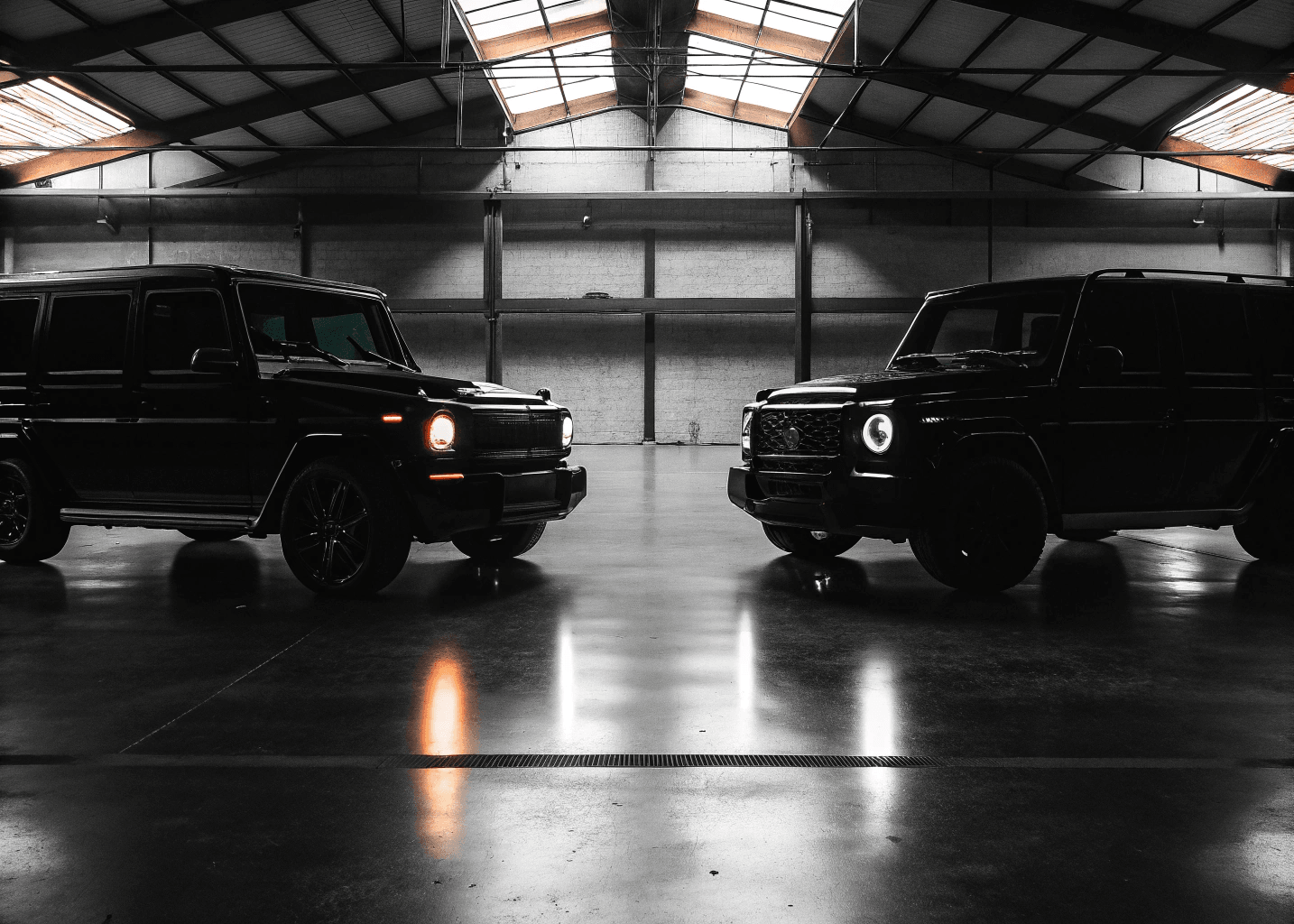 Two luxury SUVs facing each other in a dark warehouse
