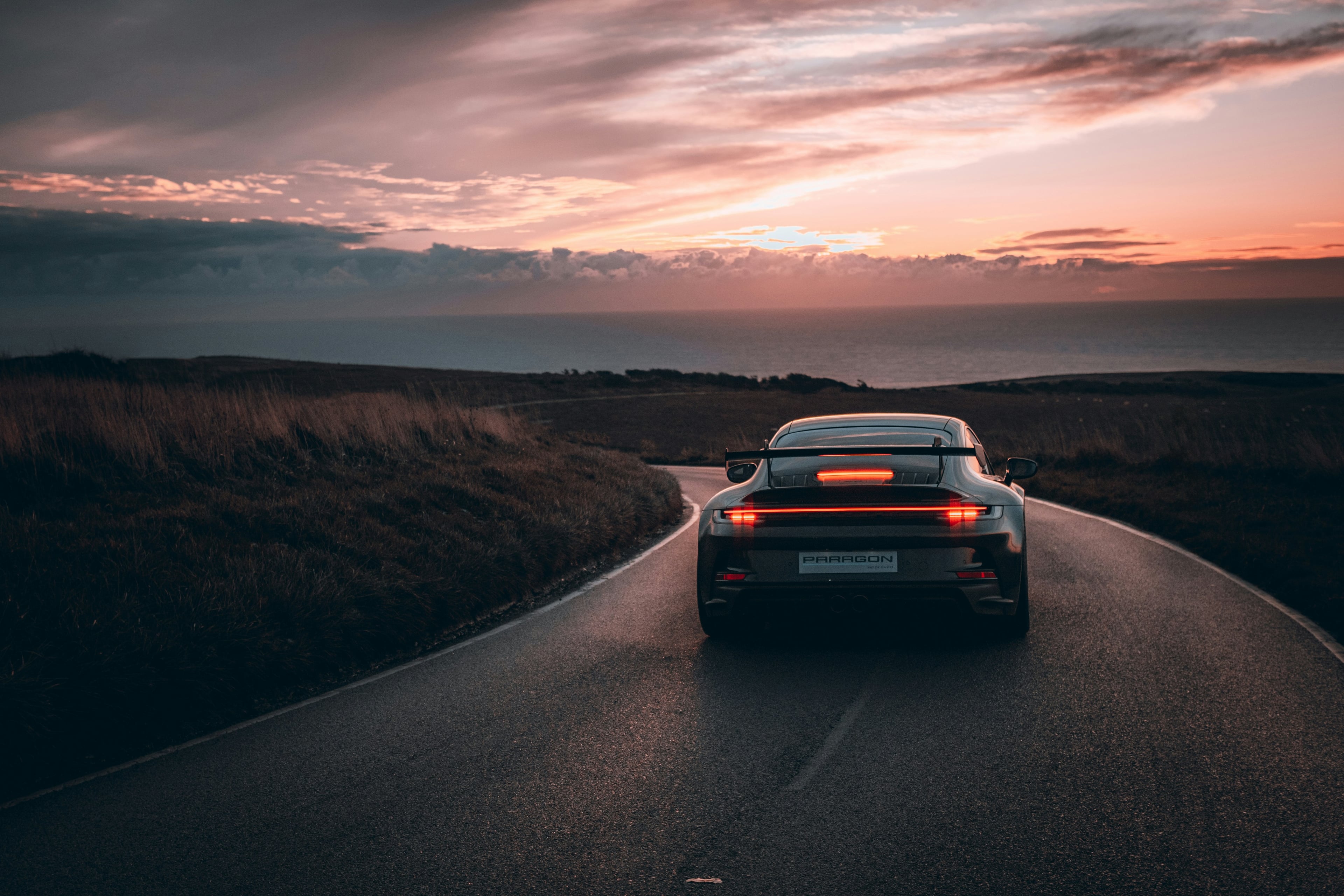 Porsche 911 GT3 cresting a coastal road at golden hour